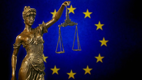 Estátua de bronze com balança na mão e símbolo da União Europeia como pano de fundo
